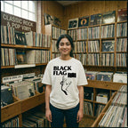 Person wearing a 'Black Flag' t-shirt in a record store filled with vinyl records.